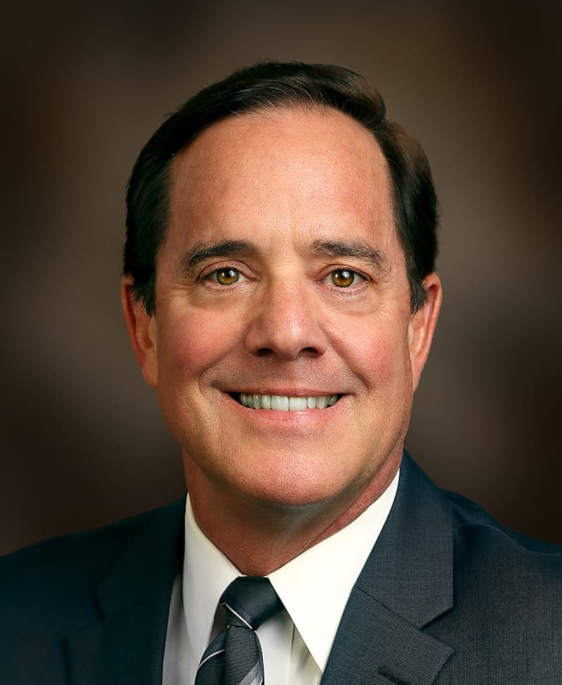 Image of Portrait of Bob Freeze, a man with short dark hair, wearing a suit and smiling against a brown background